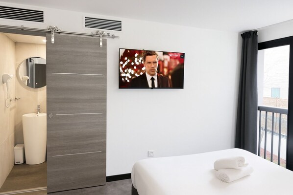 A hotel room with a bed, a TV mounted on the wall, a bathroom with a toilet, sink, and shower.