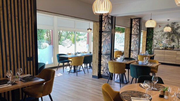 Interior de restaurante con pisos de madera, mobiliario moderno y amplios ventanales que ofrecen vistas al exterior.
