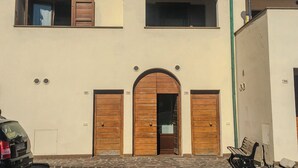 Un edificio con una entrada central en arco, dos puertas de madera, una pequeña ventana sobre la entrada y un banco en el exterior.