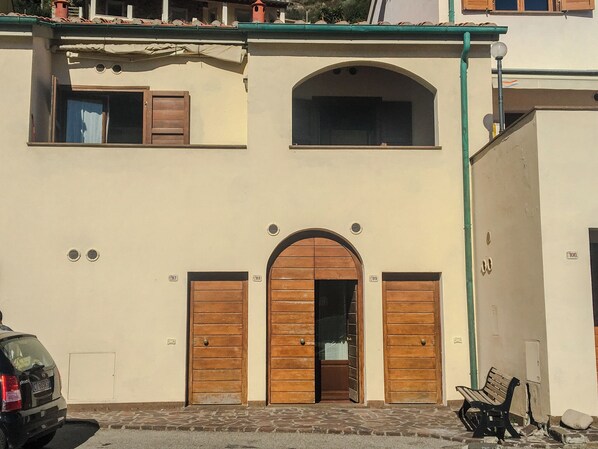 A building with a central arched entrance, two wooden doors, a small window above the entrance, and a bench outside.