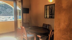 Un comedor con una mesa redonda, cuatro sillas de madera, un televisor en la pared y vistas a barcos y un paisaje montañoso a través de un amplio ventanal.