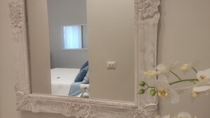 Un miroir orné de sculptures complexes, qui reflète une chambre à coucher avec un lit, des oreillers et une fenêtre avec des rideaux.
