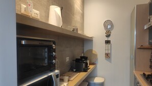 Une cuisine compacte équipée d’un four à micro-ondes, d’un four traditionnel et d’un petit plan de travail sur lequel se trouvent une machine à café et une poubelle.