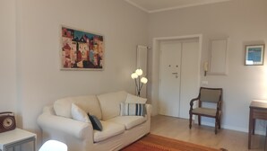 Un salon avec un canapé blanc, un tapis à motifs, une chaise en bois et un tableau accroché au mur.