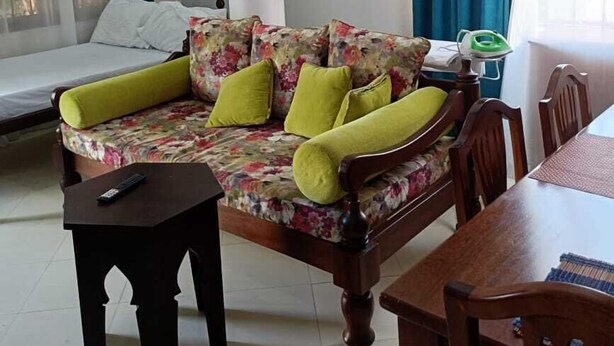 Una habitación con un sofá floral, una cama, una mesa de comedor y una mesita con un control remoto.