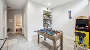 Una habitación con mesa de fútbol, máquina de videojuegos Pac-Man y estantería.