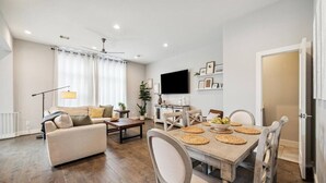 Una sala de estar moderna con un sofá, una mesa de centro, una mesa de comedor con posavasos y un televisor de pantalla plana.