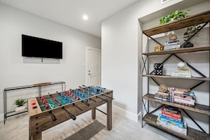 Una habitación con una mesa de fútbol de mesa, una estantería llena de libros y un televisor en la pared.