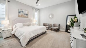 Un dormitorio con cama, mesitas de noche, ventilador de techo, espejo y escritorio con un jarrón de flores.