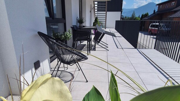 A modern outdoor patio with a dining area, a staircase, and a view of a mountain. - BERGLIEBE (Kaprun)