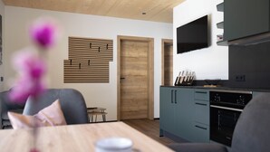 A modern kitchen with a built-in oven, a dining area with a table and chairs, and a wooden door. - BERGLIEBE (Kaprun)