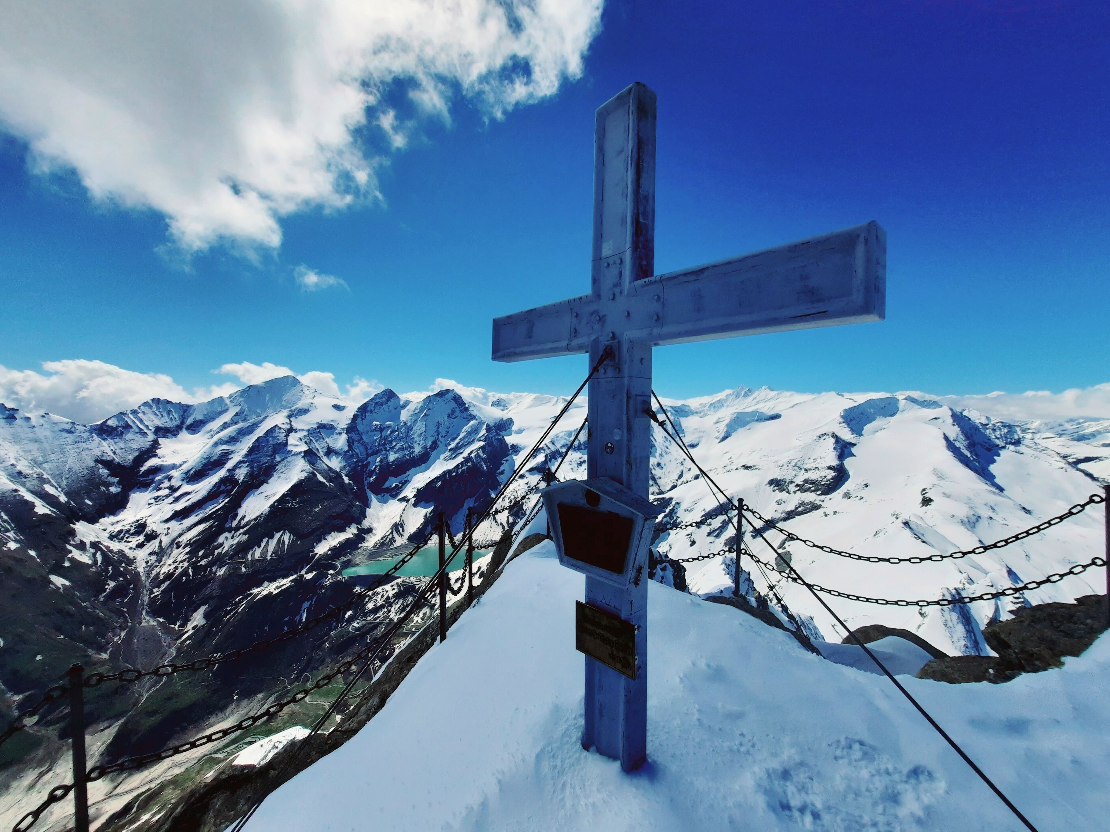 A snow-covered mountain with a cross at the peak, surrounded by chains and a clear sky.