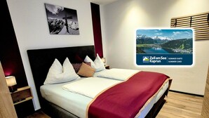 A modern hotel room with a large bed, a nightstand, a wall-mounted TV, and a wooden floor. - BERGLIEBE (Kaprun)