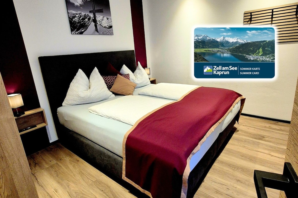 A modern hotel room with a large bed, a nightstand, a wall-mounted TV, and a wooden floor.