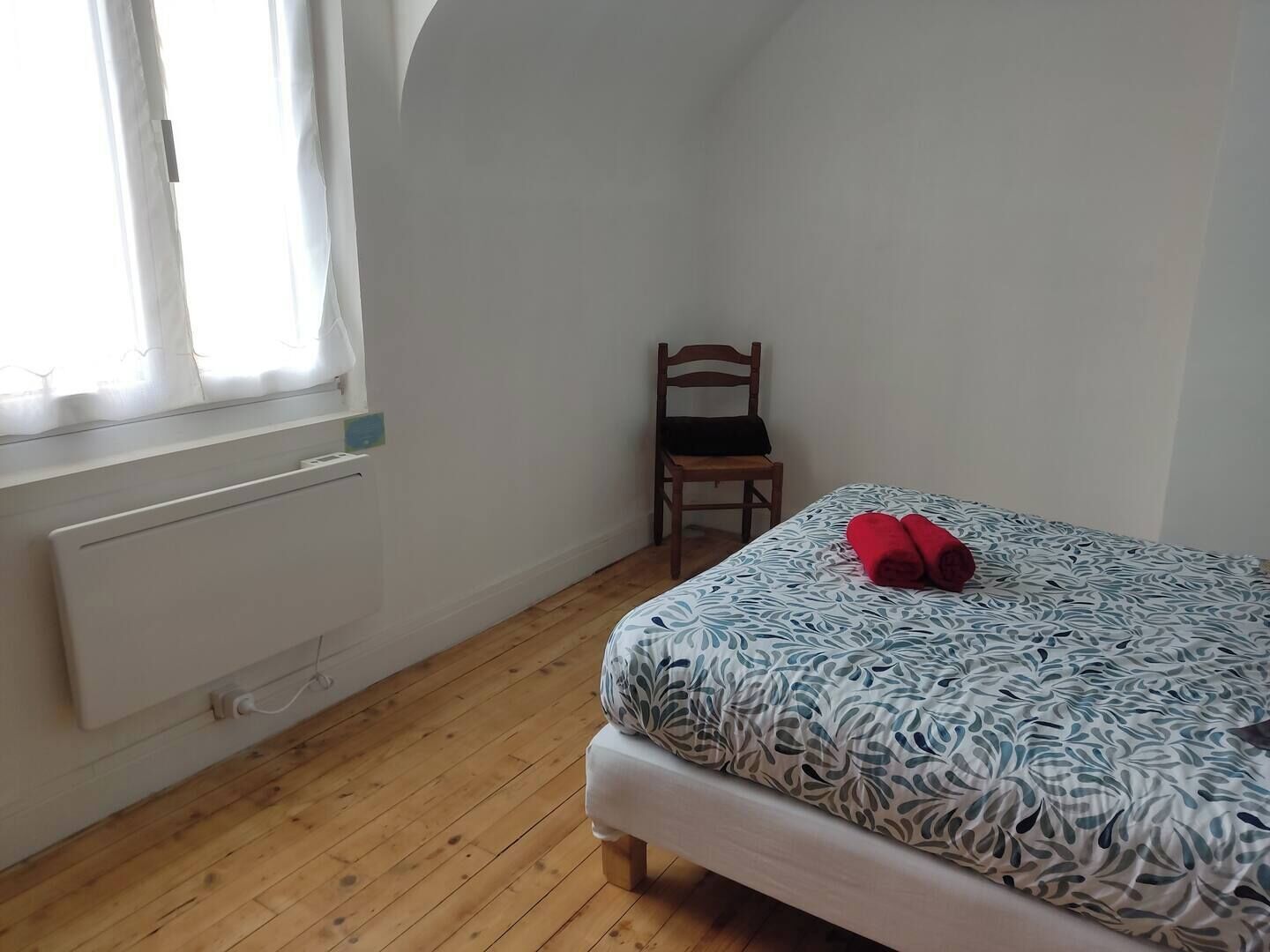 A small, tidy room with a bed, a chair, and a radiator.
