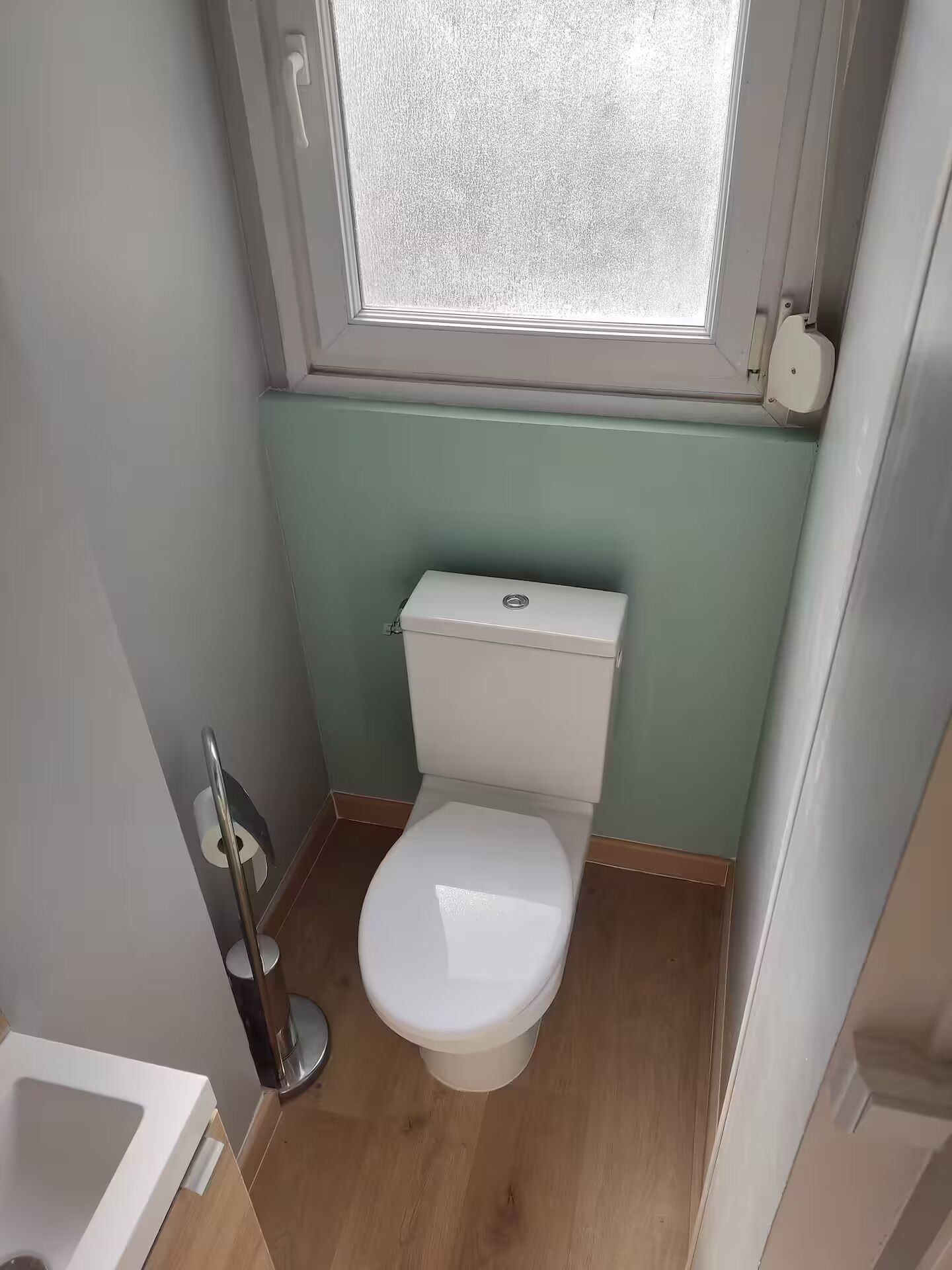 A small bathroom with a toilet, a window, and a toilet paper holder.