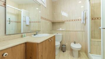 Baño con tocador de madera, dos inodoros, un lavamanos, un espejo y una ducha.