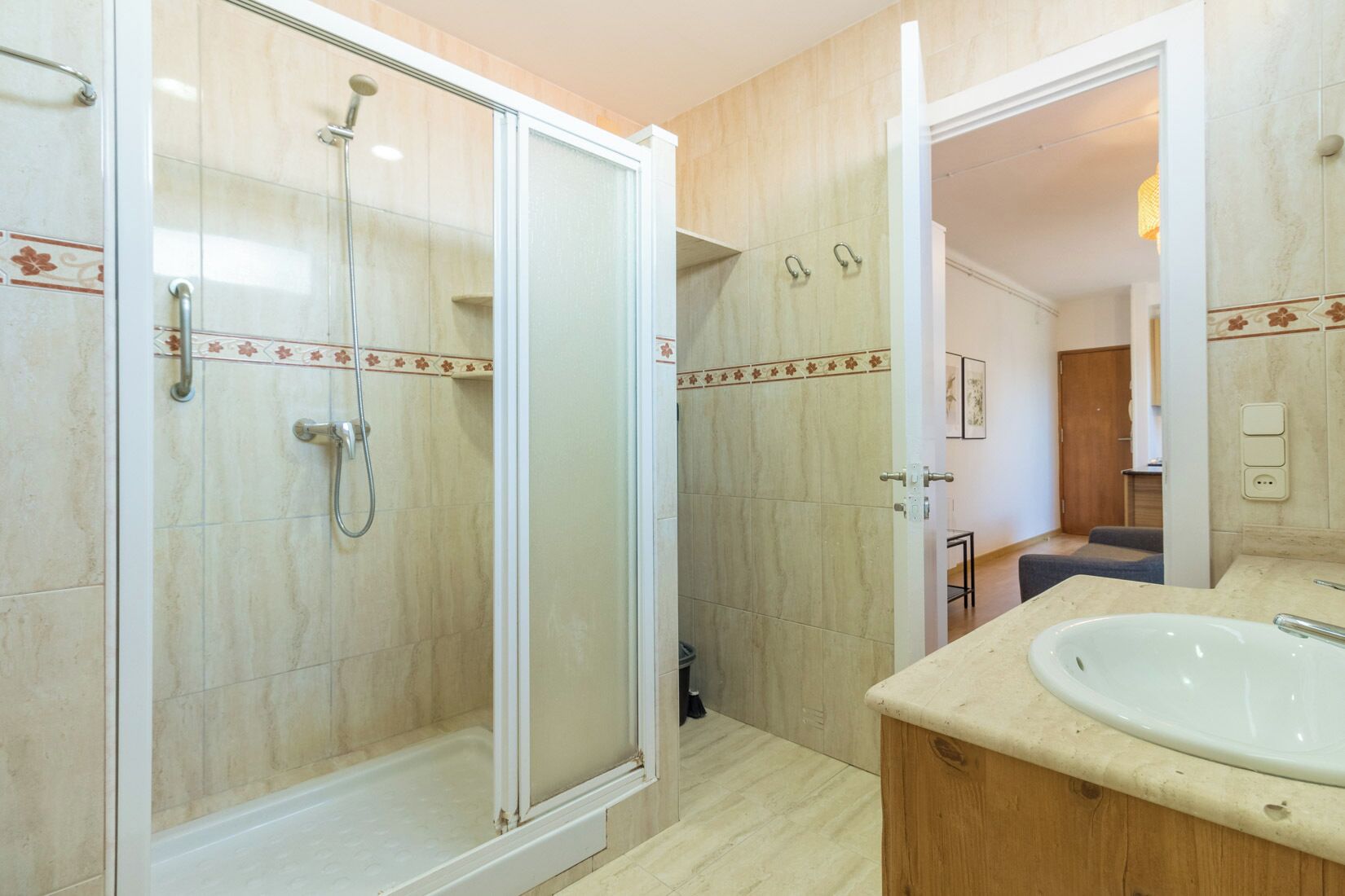 A bathroom with a glass-enclosed shower, a wooden vanity with a sink, and a tiled floor.