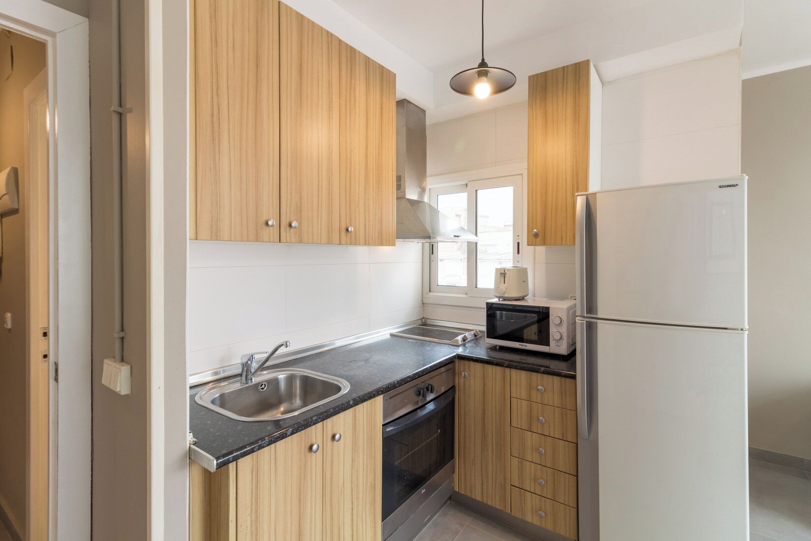 Eine moderne Küche mit Holzschränken, einer Edelstahl-Spüle, einer Mikrowelle und einem Kühlschrank.