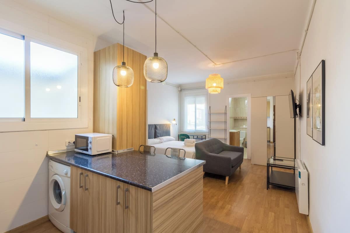 A compact kitchen with a washing machine, a microwave, and a small dining area with a chair and table.