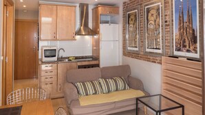 Een ruimtelijk ingerichte leefruimte met kitchenette, een bank, een glazen salontafel en een eethoek met een houten tafel en stoelen.