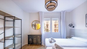 A bedroom with a bed, a wardrobe, a mirror, and a window with a view of buildings. - BeBarceloner Eixample Apartments (Barcelona)