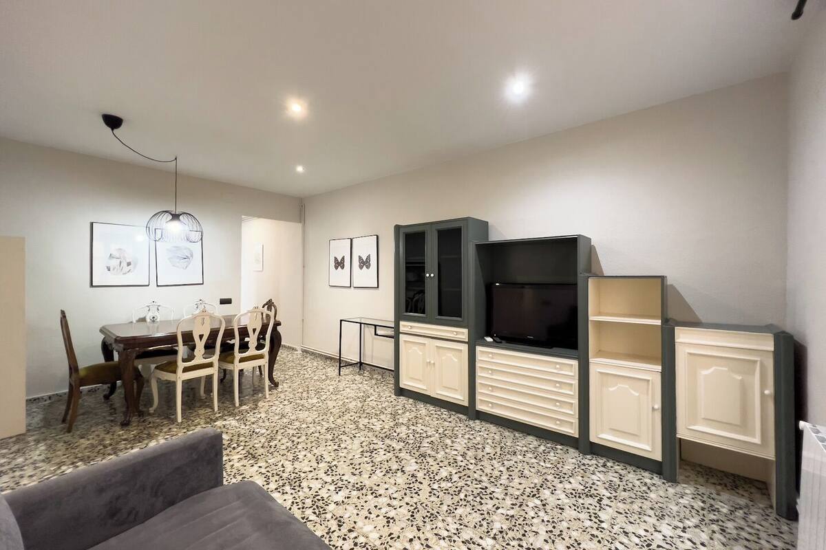 A modern living room with a dining area, featuring a TV, cabinets, and artwork on the walls.