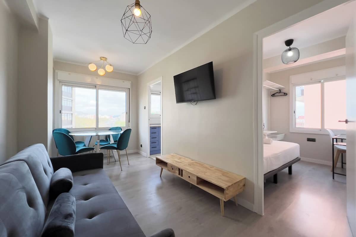 Eine moderne Wohnung mit Wohnbereich, Essplatz und Schlafzimmer. Sie verfügt über ein großes Fenster, einen Flachbildfernseher und eine Holzbank.