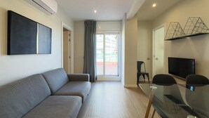 Un salon moderne avec un canapé gris, une table en verre, un téléviseur à écran plat et un balcon avec vue.