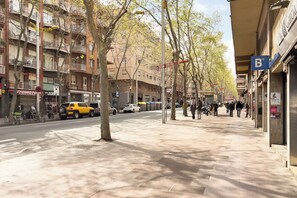 A street with parked cars, a yellow taxi, and pedestrians.