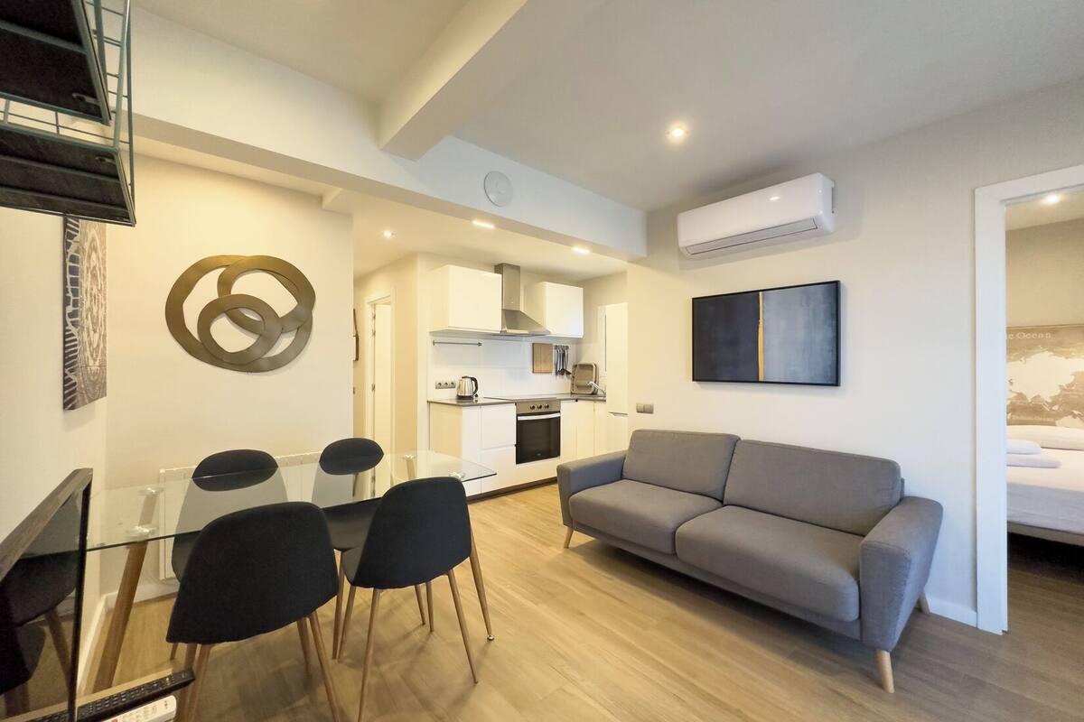 Eine moderne Wohnung mit Essbereich, einem grauen Sofa und einer Küchenzeile.