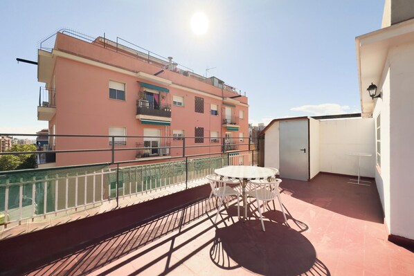 Eine Dachterrasse mit Tisch und Stühlen, einer weißen Tür und einem rosafarbenen Gebäude im Hintergrund.