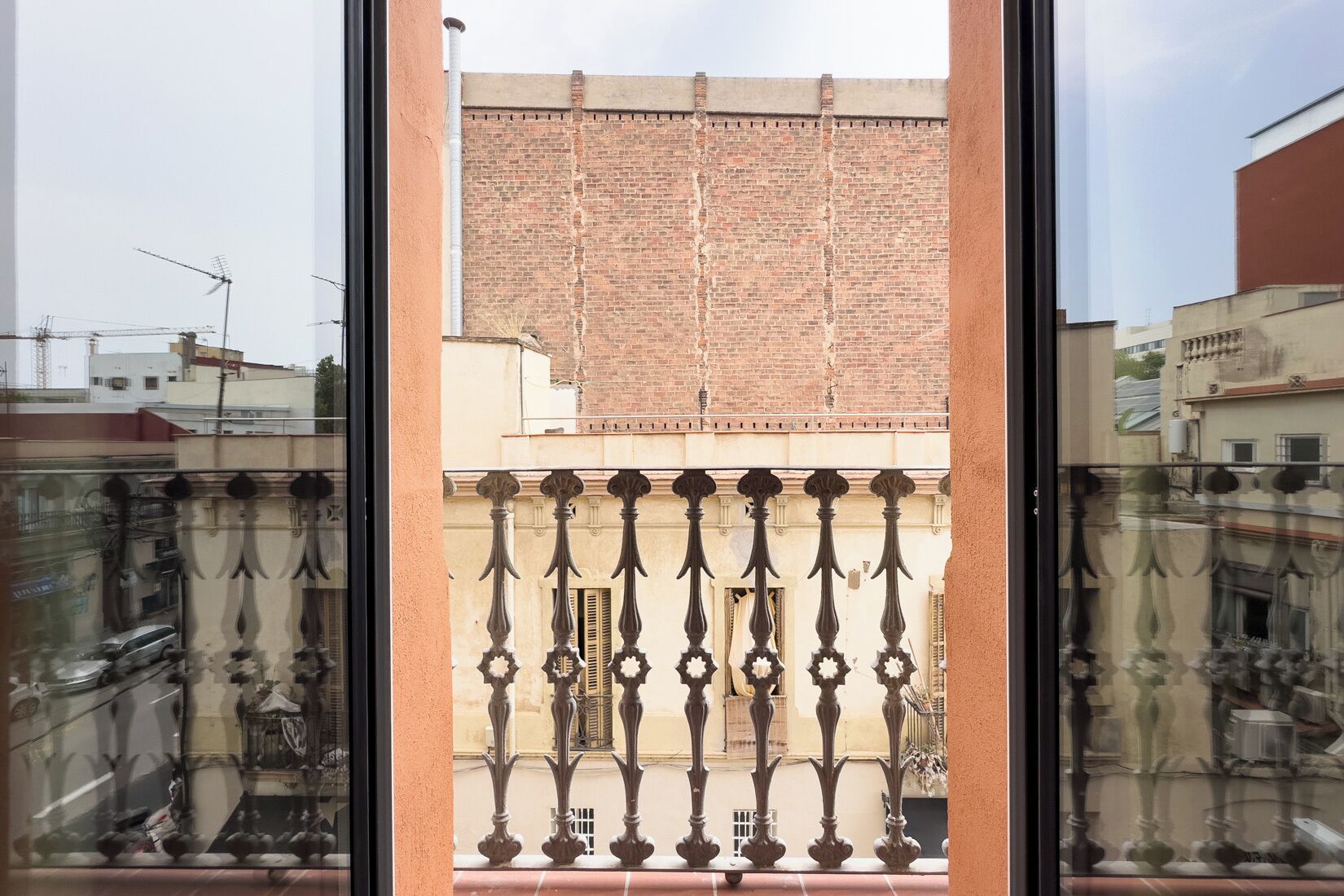 Blick durch ein Fenster mit Balkonbrüstung, ein Ziegelgebäude und ein klarer Himmel.