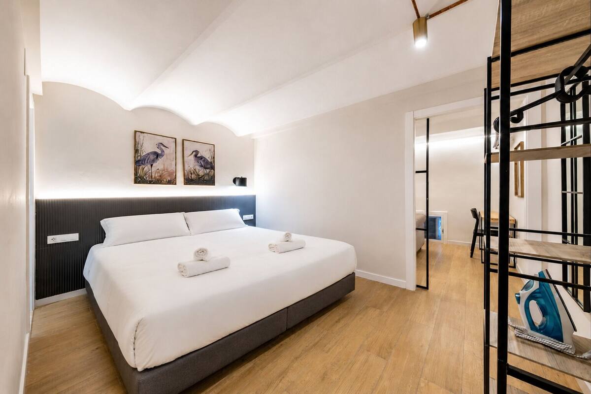 Egy modern szállodai szoba, amelyben egy nagy ágy, parketta, egy íróasztal székkkel és a háttérben egy emeletes ágy található.
