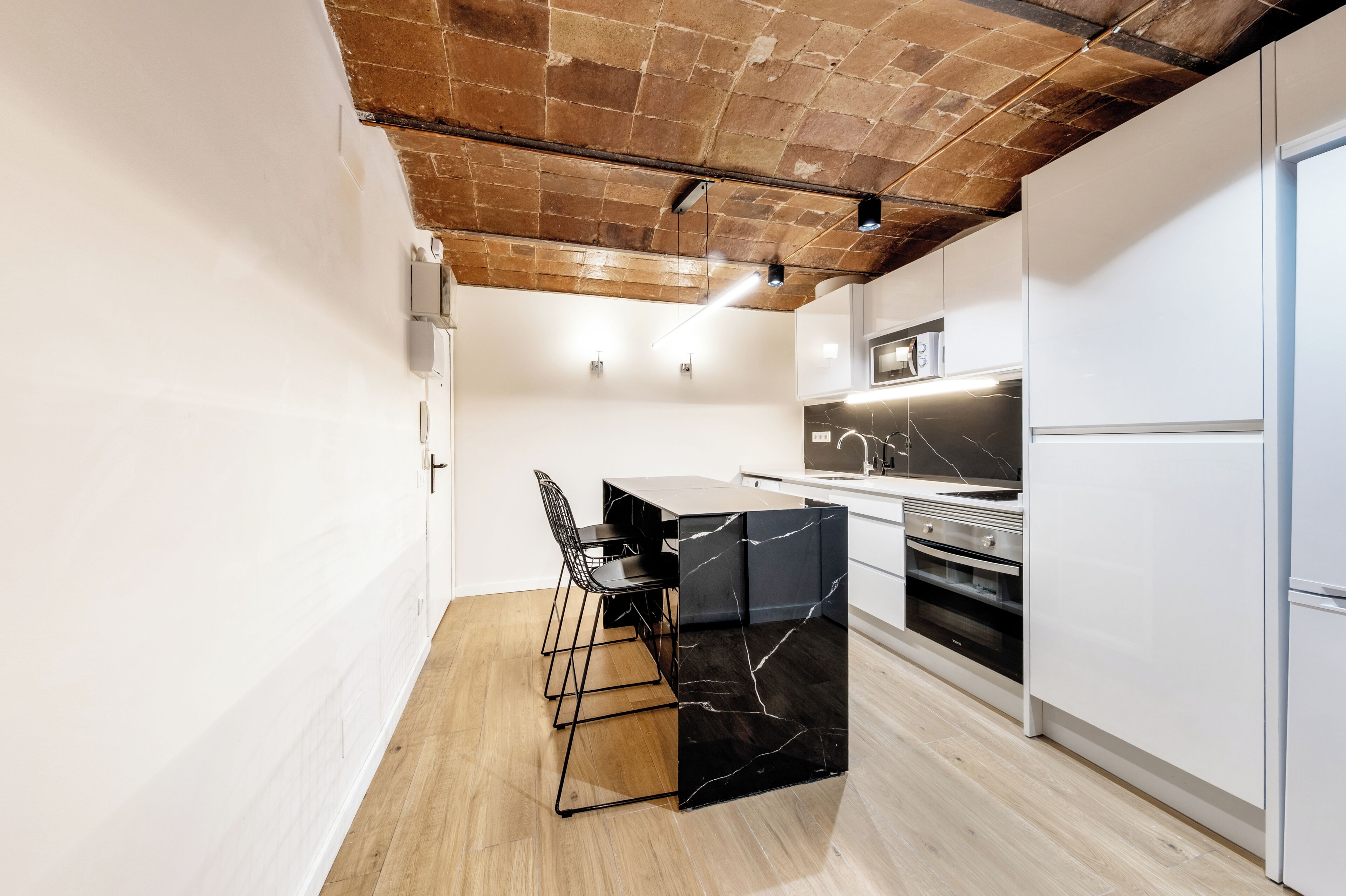 Una cucina moderna con isola in marmo, soffitto in legno e mobili bianchi.