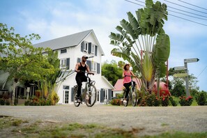 Dos personas montando en bicicleta por una calle, con casas y una señalización al fondo.