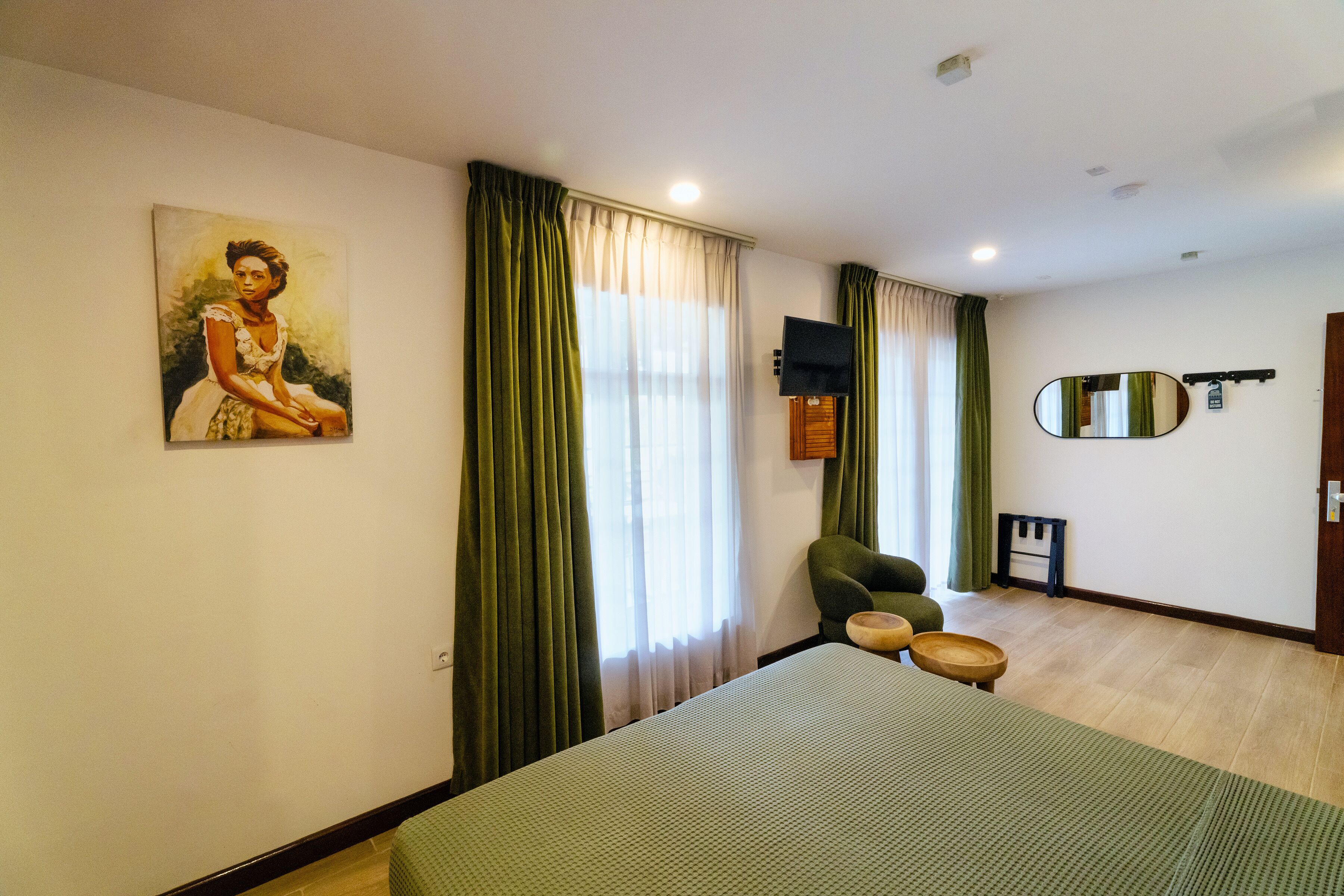 A hotel room with a bed, a chair, a painting, a television, and a mirror.