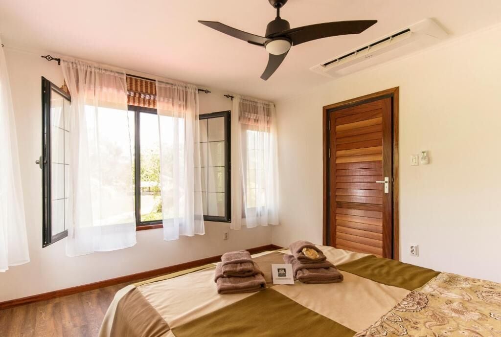 A room with a bed, a ceiling fan, a window with curtains, and a wooden door.