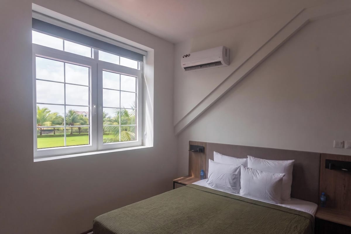 Un dormitorio con cama, ventana, aire acondicionado y vistas a zonas verdes.