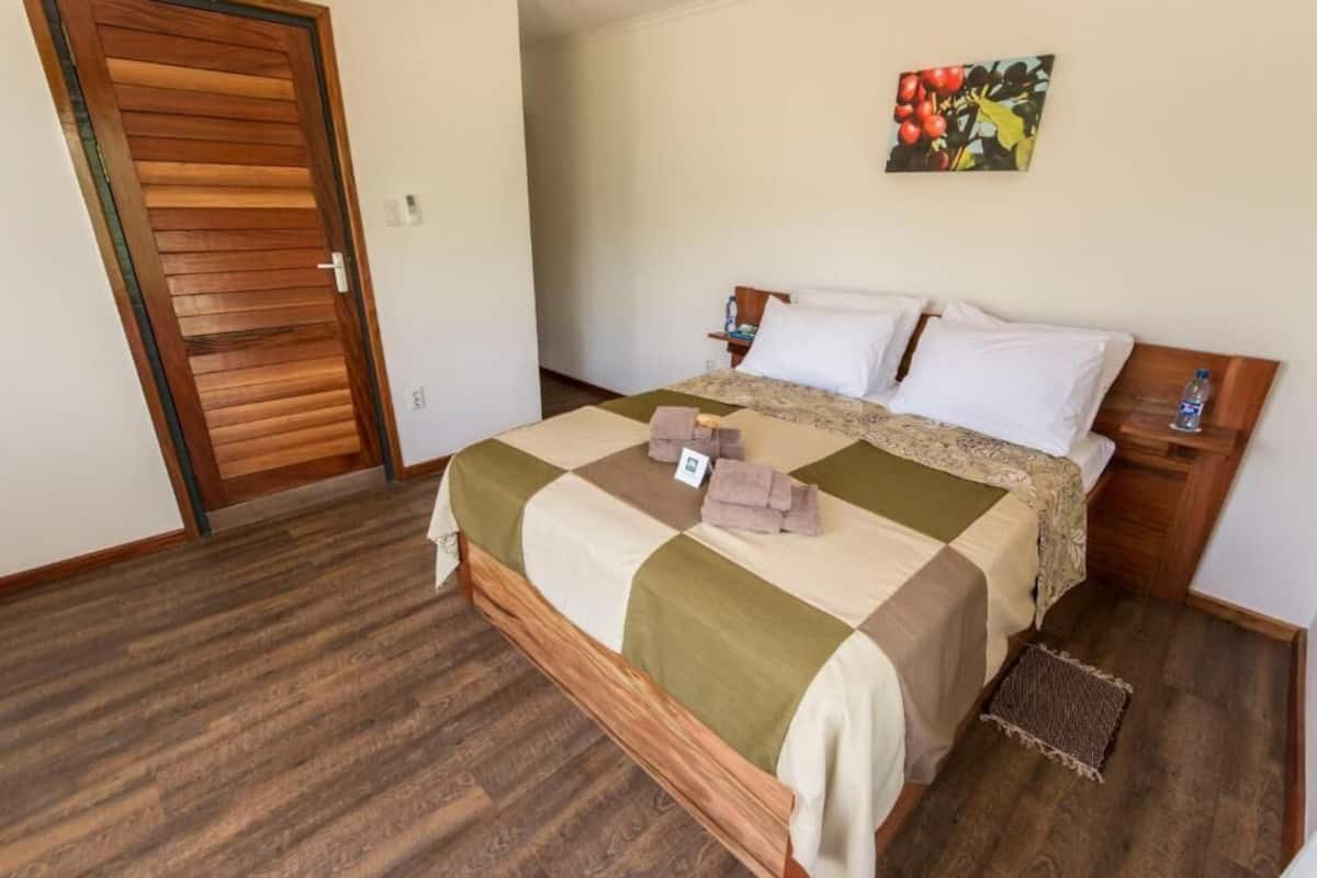 Un dormitorio con una cama de madera, colcha a cuadros, un cuadro en la pared y suelo de madera.