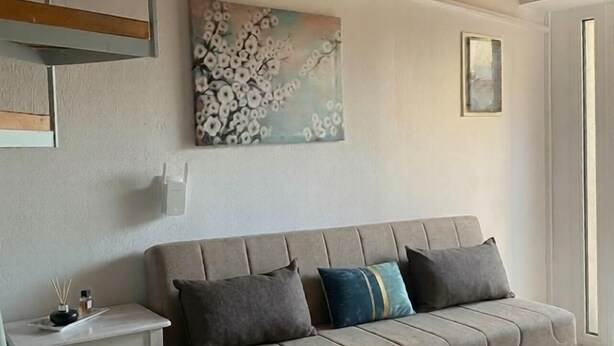 A modern living room with a beige sofa, a small white side table, and a painting on the wall.