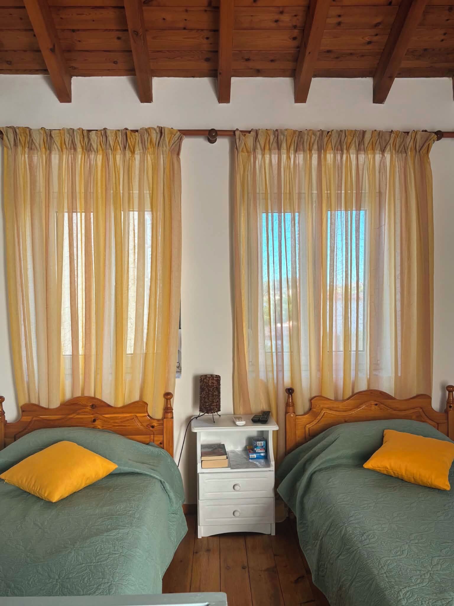 Una habitación con dos camas de madera, una mesita de noche y cortinas.