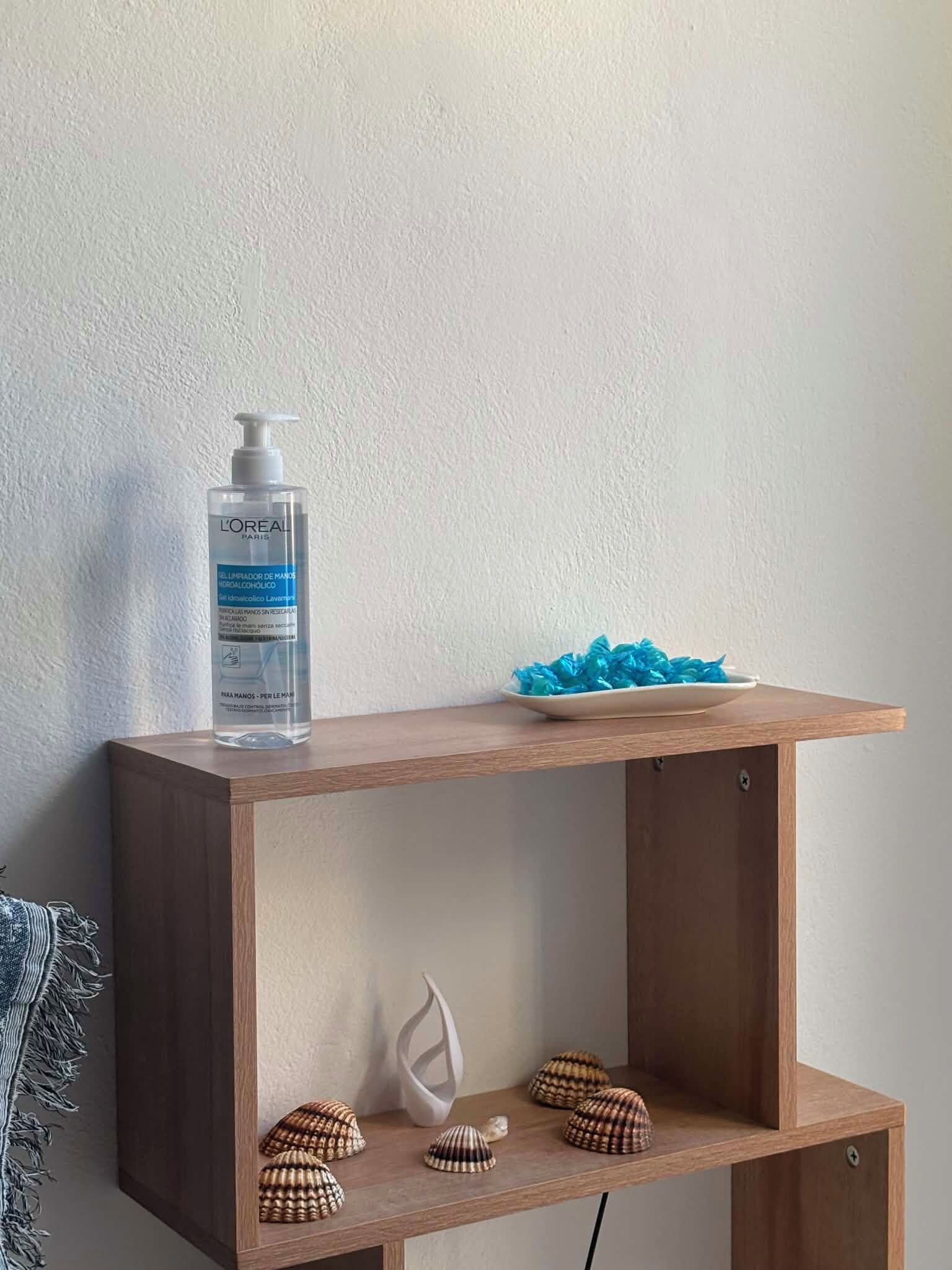 Una estantería de madera con una botella de jabón de manos L'Oréal y caracolas decorativas.