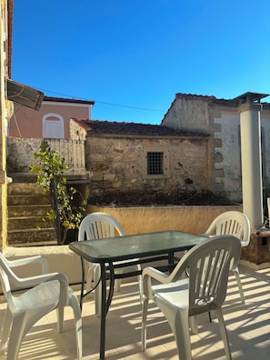Eine Terrasse im Freien mit Tisch und Stühlen, eine Steinmauer und ein Gebäude mit Fenster und Tür.