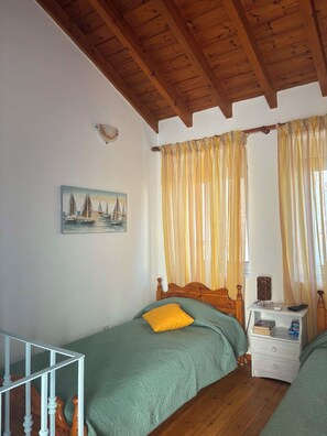Ein Schlafzimmer mit zwei Einzelbetten, Holz-Kopfteilen, einem Bild an der Wand und einem Fenster mit Vorhängen.