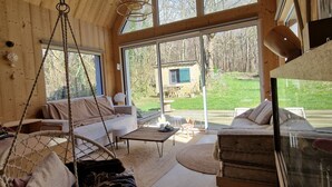 A cozy cabin interior with a large window, a hanging chair, and a sofa. - Quiet lodge in Wissant, in the forest and 500m from the beach.  Ideal for a couple (Wissant)