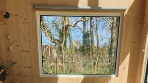 A cozy bedroom with a large window, a bed with pillows, and a view of trees. - Quiet lodge in Wissant, in the forest and 500m from the beach.  Ideal for a couple (Wissant)