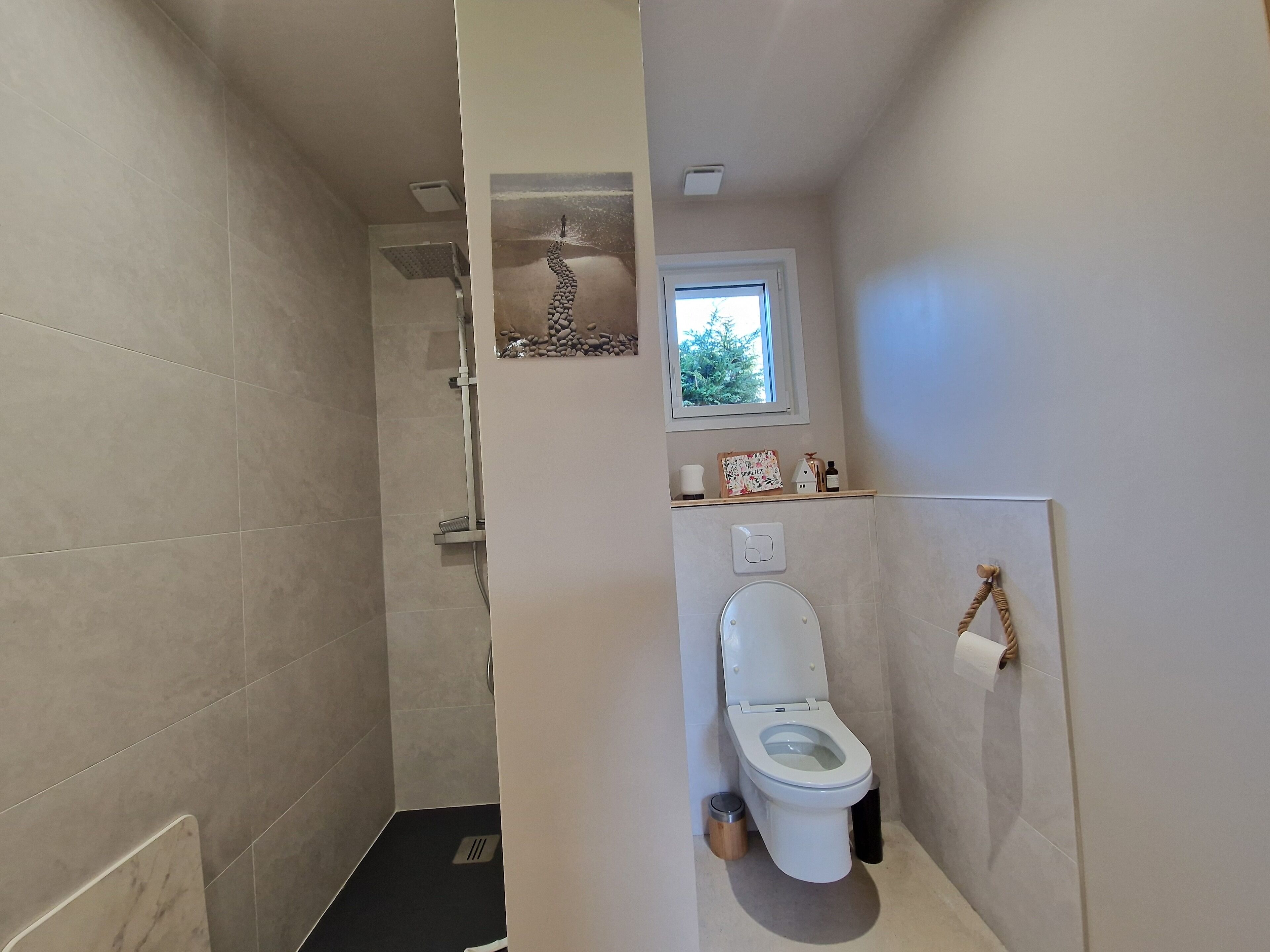 A bathroom with a shower, toilet, and a small window.