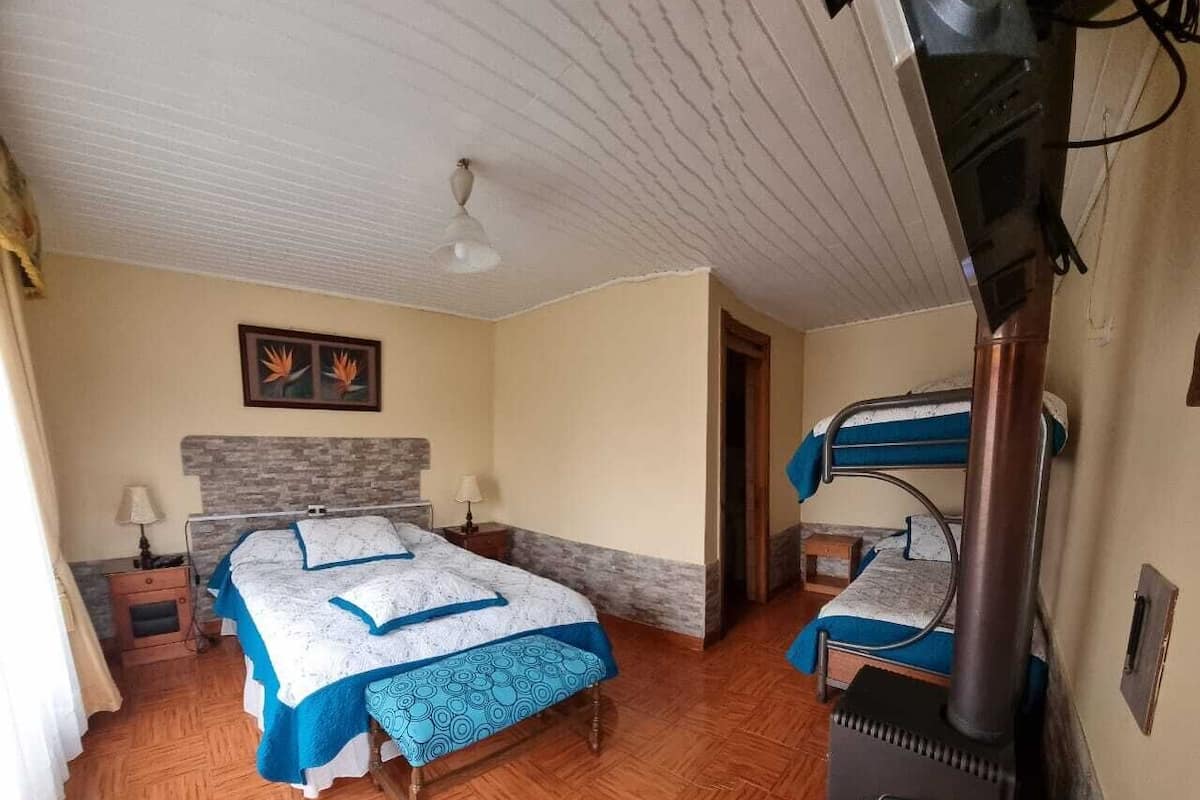 A bedroom with a bed, a heater, and a small table with a lamp.