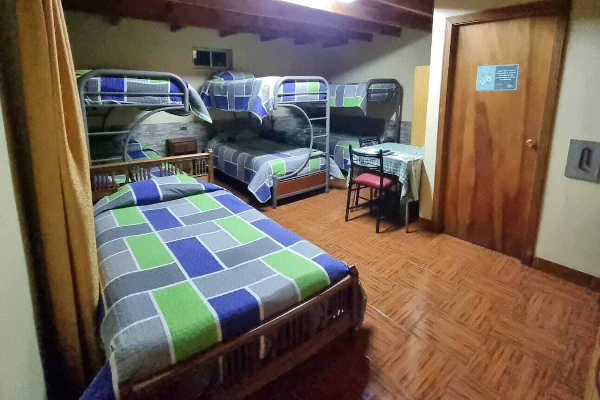 A room with three bunk beds, wooden flooring, a small desk, and a door with a sign.